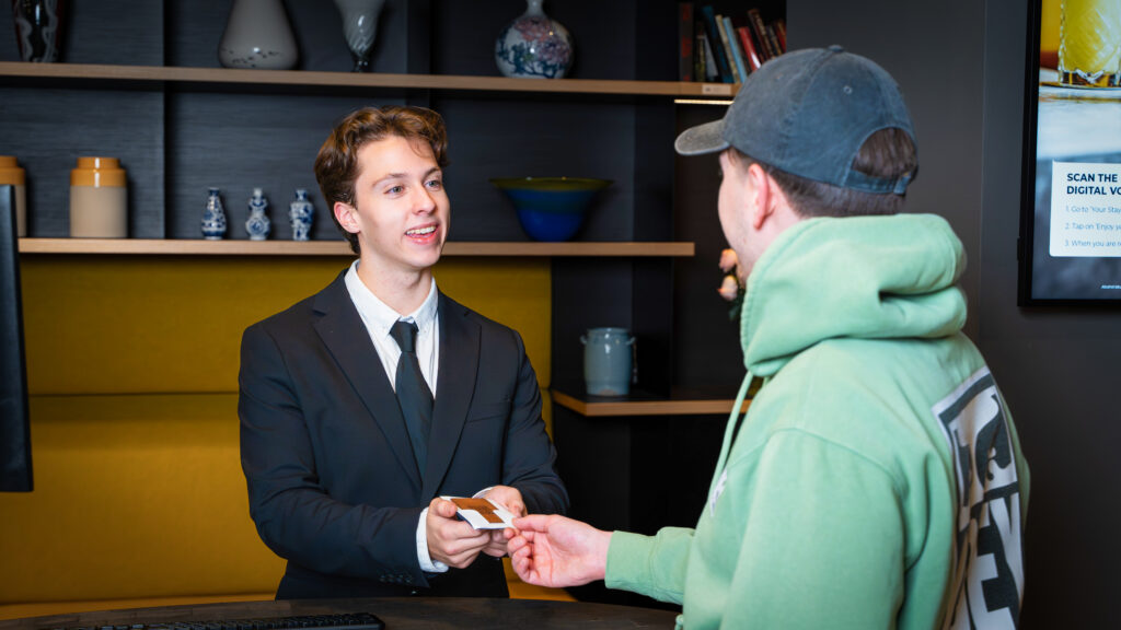 Nachtreceptionist die een toegangspasje overdraagt tijdens de professionele overdracht en daarmee betrouwbare nacht receptie services biedt voor veilige 24/7 hotelservice.